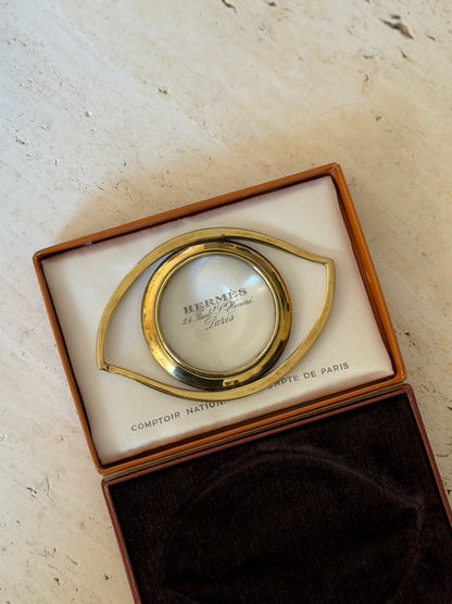 Hermes gilt magnifier laid on the satin lining of its box, the round lens enlarging the Hermes 24 Faubourg Saint-Honore Paris imprint