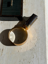 Overhead view of the Hermes magnifier on travertine, sunlight focused through the round lens beside a dark lacquered box