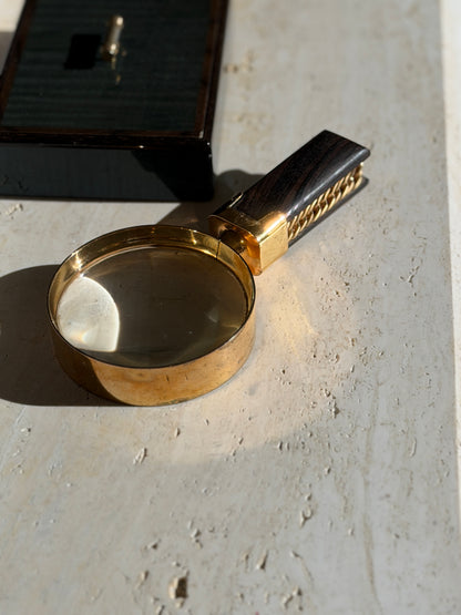 Angled view of the deep gilt lens rim and square collar, the striped ebony handle with chain detail running behind