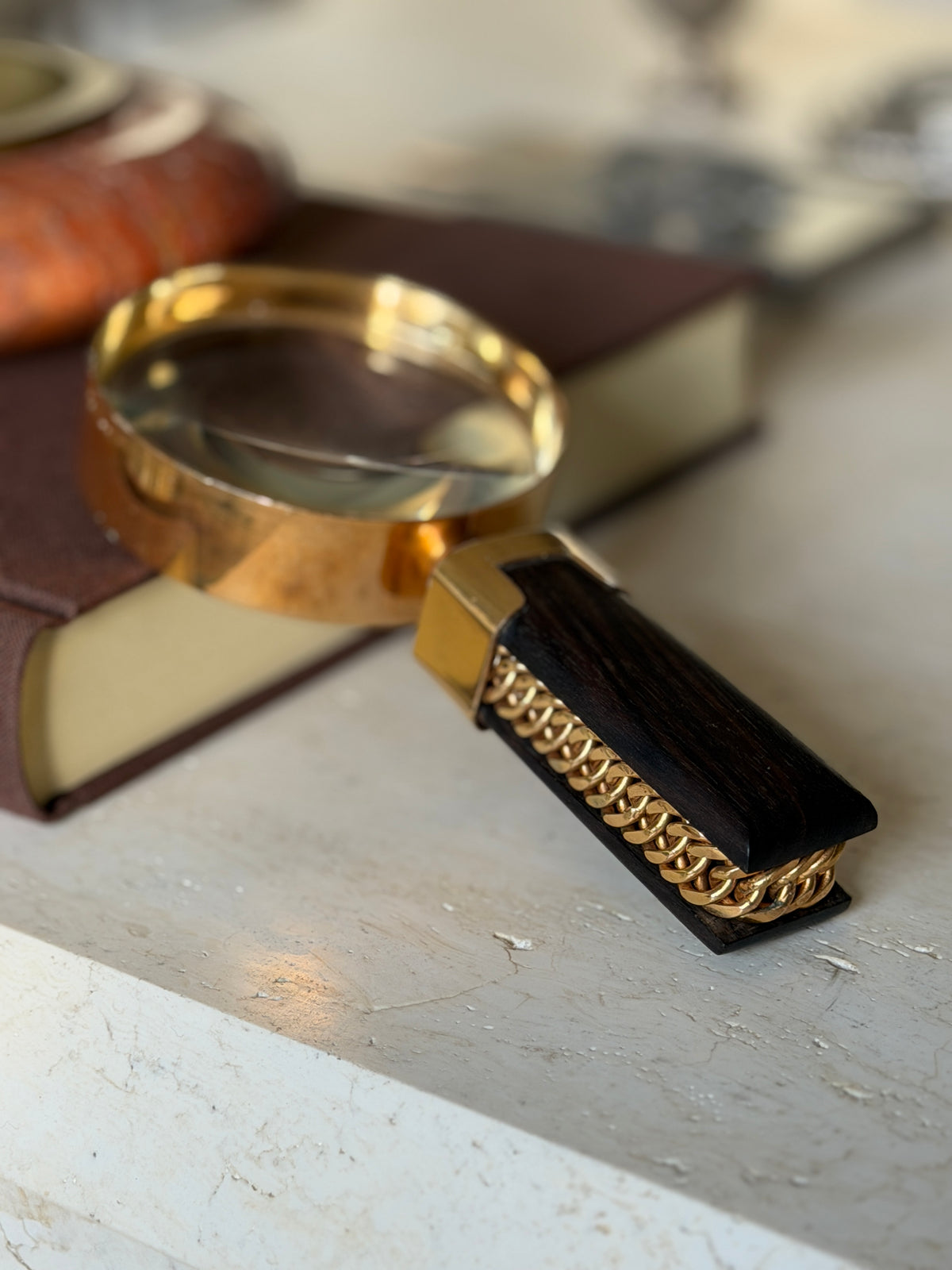 Close side view of the ebony and gilt chain link handle in sharp focus, the deep polished lens rim showing light wear to the gilding along its edge
