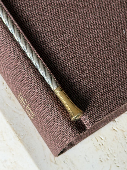 Detail of a gilt stirrer tip stamped HERMES at the collar, the twisted silver cable stem resting on a brown book