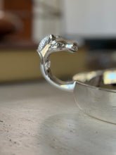 Profile close-up of the sculpted horse head handle curving over the rim of the silver catchall
