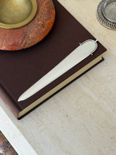 Hermes spur letter opener resting on a brown clothbound book beneath a red stone ashtray with brass insert