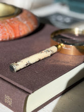 Close view of the handle end cap and inlaid leaves on the Hermes magnifier, a red stone ashtray softly blurred behind