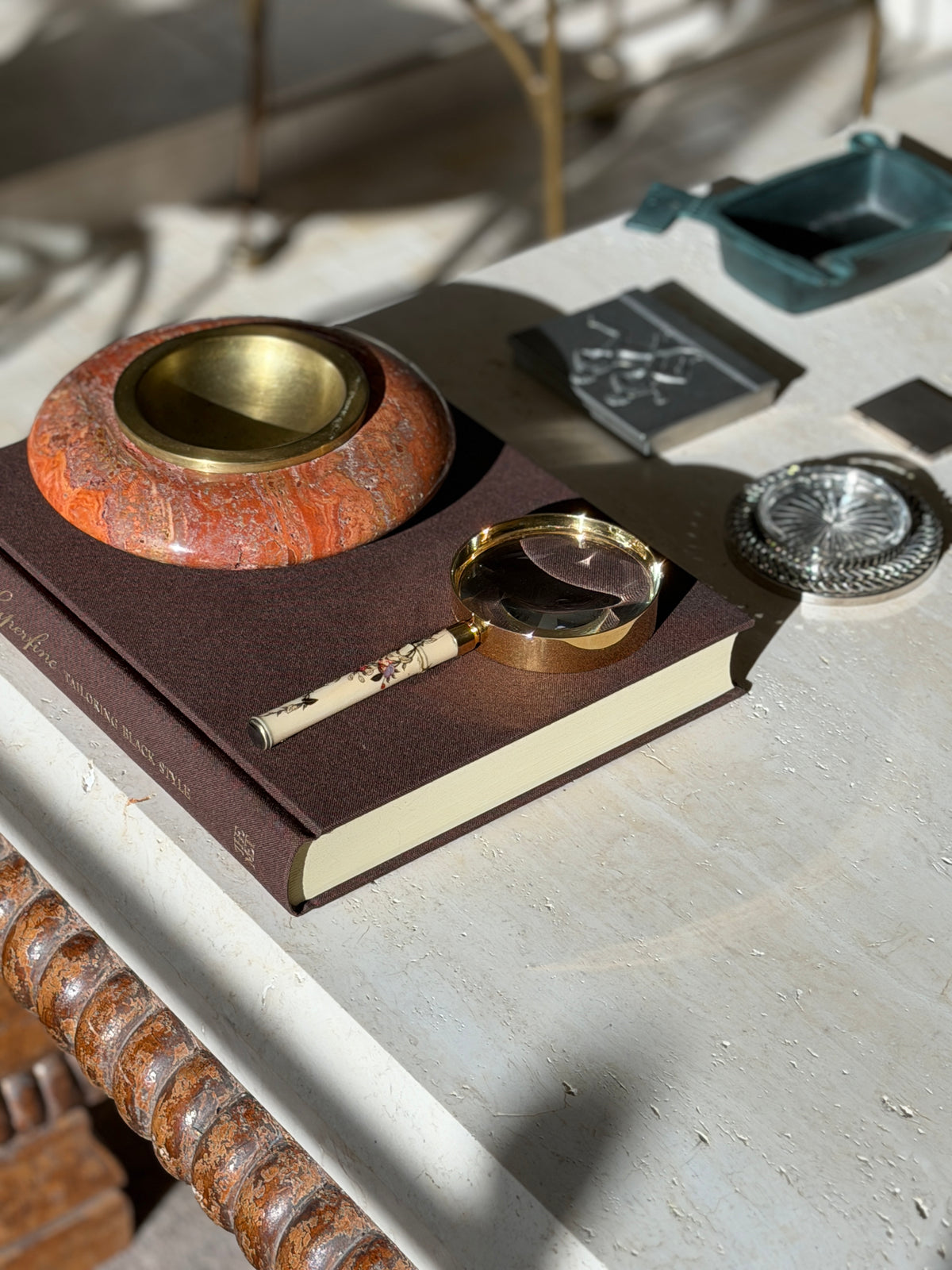 Hermes magnifying glass styled on a travertine console with a red stone ashtray, a silver coaster, and a bronze tray