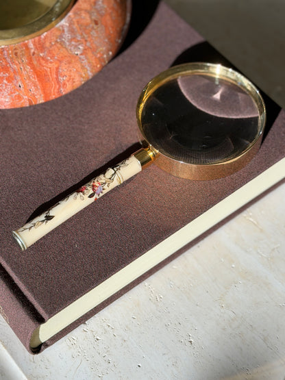 Hermes magnifying glass on a brown clothbound book in strong sunlight, beside a red travertine ashtray with a brass insert