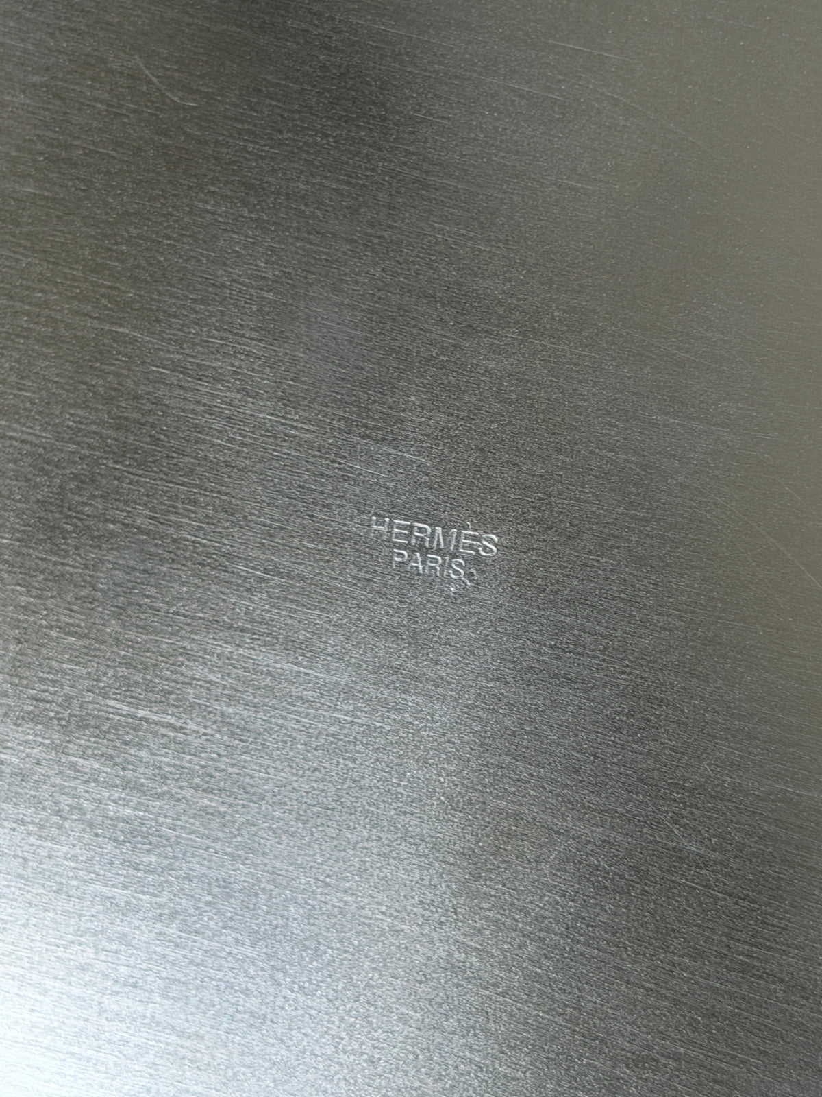 Close up of the coaster underside stamped HERMES PARIS in small capitals on brushed silver