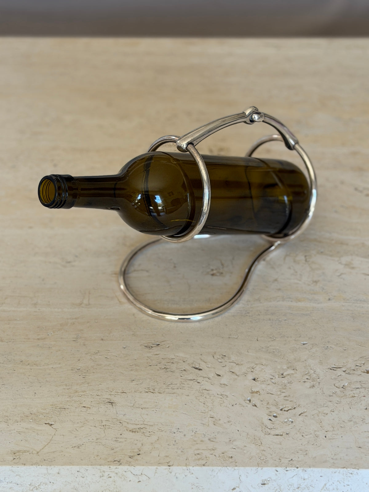 Side view of a green wine bottle cradled in the Hermes horse bit caddy, the two rings supporting the neck and base