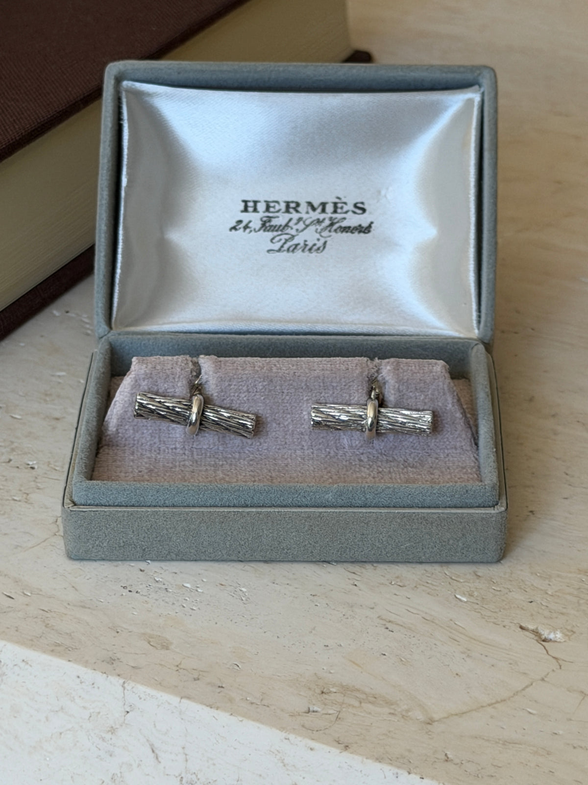 Front view of the open Hermes box with both rope bar cufflinks seated on the cushion below the satin lid lining