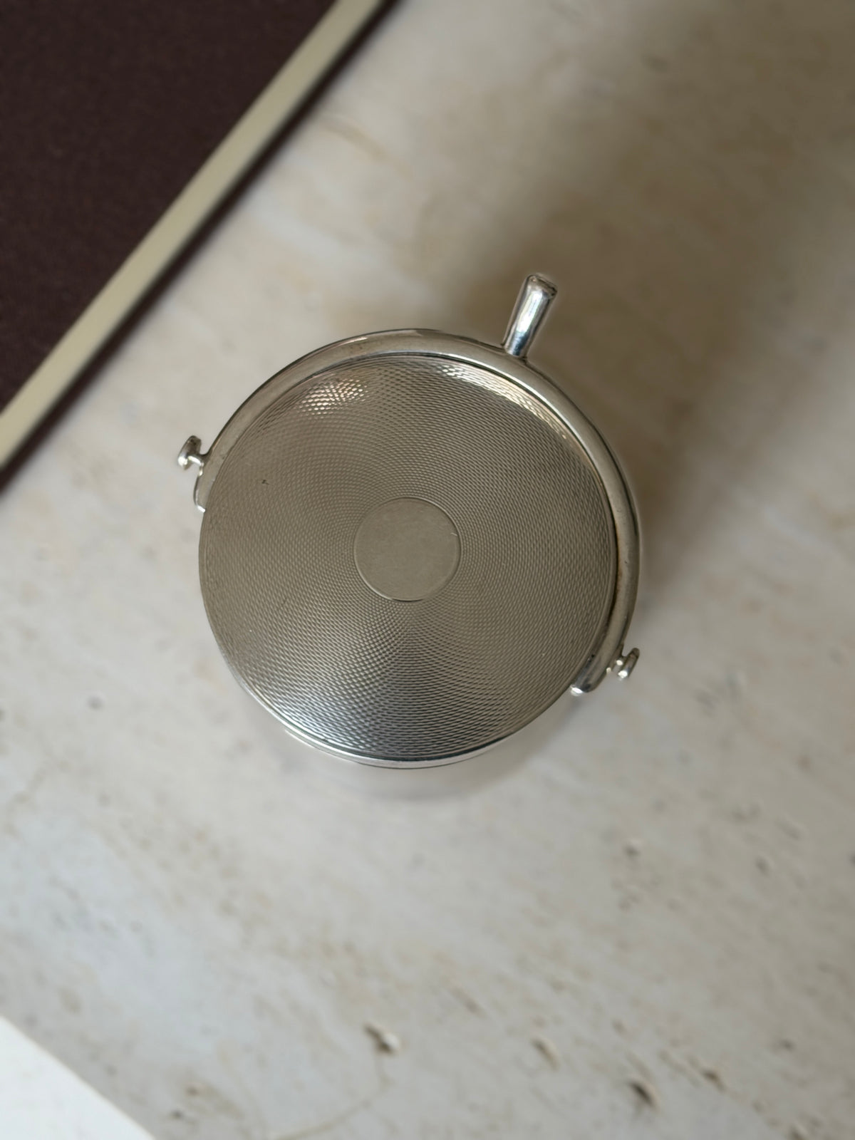 Overhead view of the guilloche lid with its smooth central cartouche, the curved spur handle and button ends framing one side
