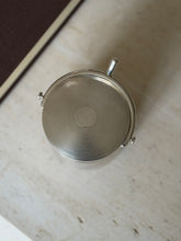 Overhead view of the guilloche lid with its smooth central cartouche, the curved spur handle and button ends framing one side