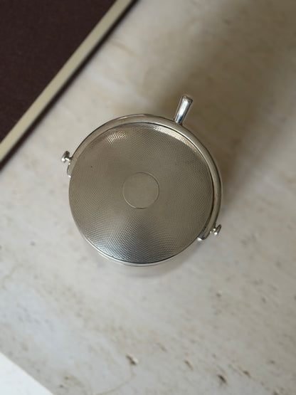Overhead view of the guilloche lid with its smooth central cartouche, the curved spur handle and button ends framing one side