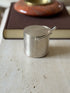 Eye level view of the sterling spur box on travertine, the spur neck curving up from the handle in front of a brown book and red stone ashtray