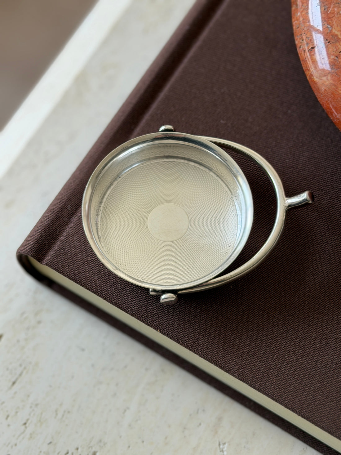 Hermes silver spur catchall on the corner of a brown book beside a red stone ashtray, the curved hoop ending in a short spur neck