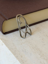 Stirrup money clip standing against a brown book on travertine, the worn patina showing along the plain outer loop