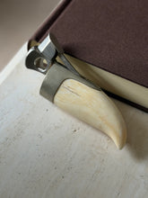 Whale tooth cigar cutter propped against a book spine, the cutting ring and spring lever opened above the silver mount
