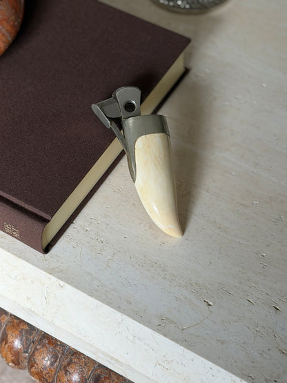 Hermes whale tooth cigar cutter on a travertine console beside a brown book, the open blade showing its round cutting aperture