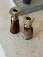 Angled overhead view of pair of horn and silver modern candlestick holders styled on table surface