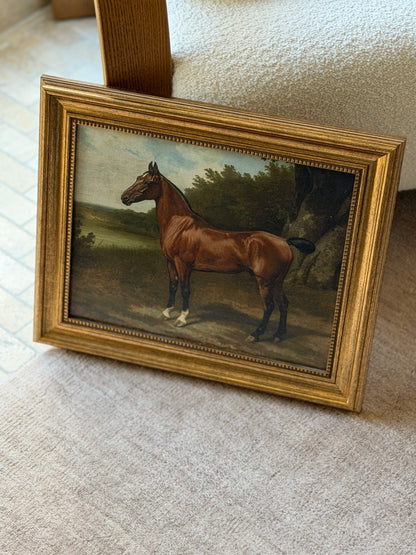 Horse in Landscape equestrian print in a reeded gilt frame leaning against an oak armchair, a bay with white socks standing beside a lake under a large tree