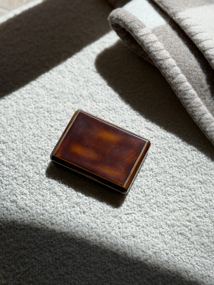 Keller Paris lacquer box on a cream boucle surface in raking sunlight, light surface wear visible on the polished lid