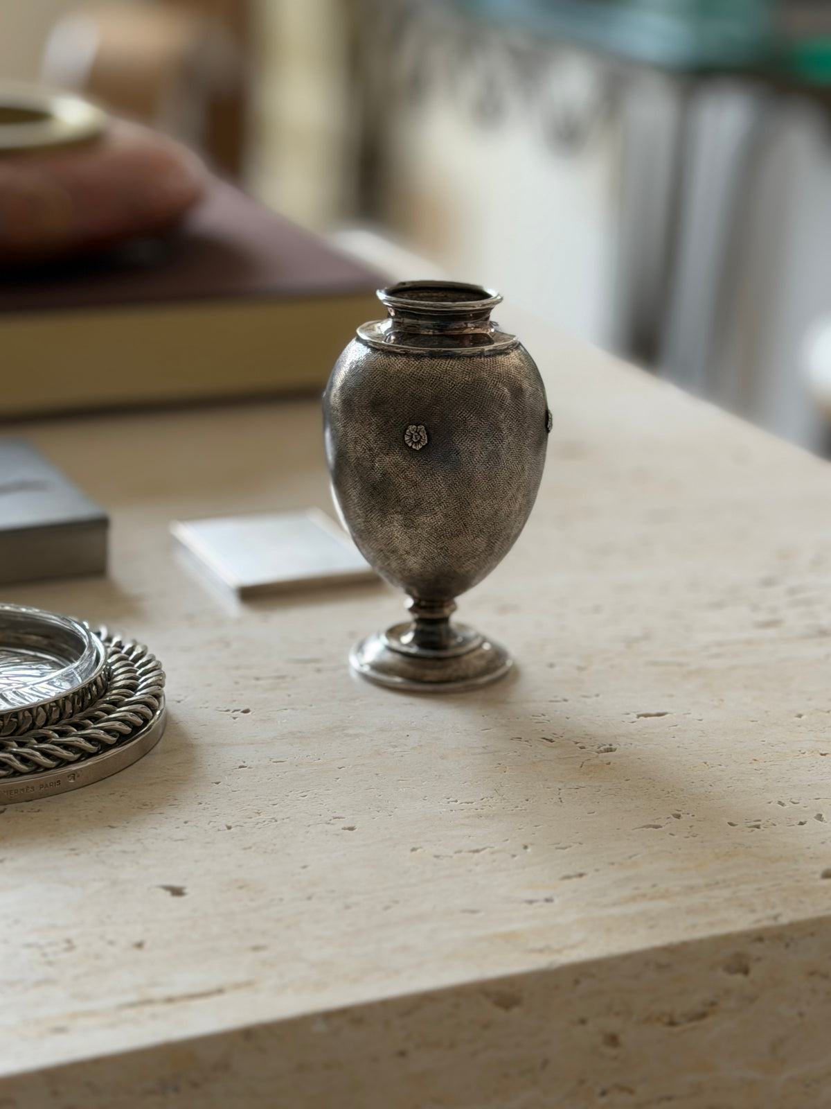 Eye level view of the Buccellati vase on a pedestal foot, the woven texture surface and small silver rosette catching light
