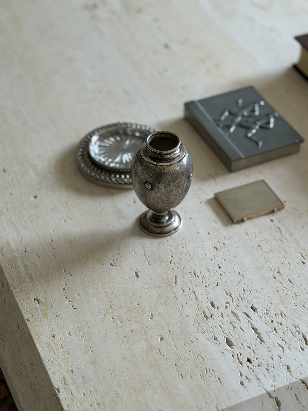 High angle view of the Buccellati vase beside a silver chain coaster with glass insert and a pewter box with runners in relief