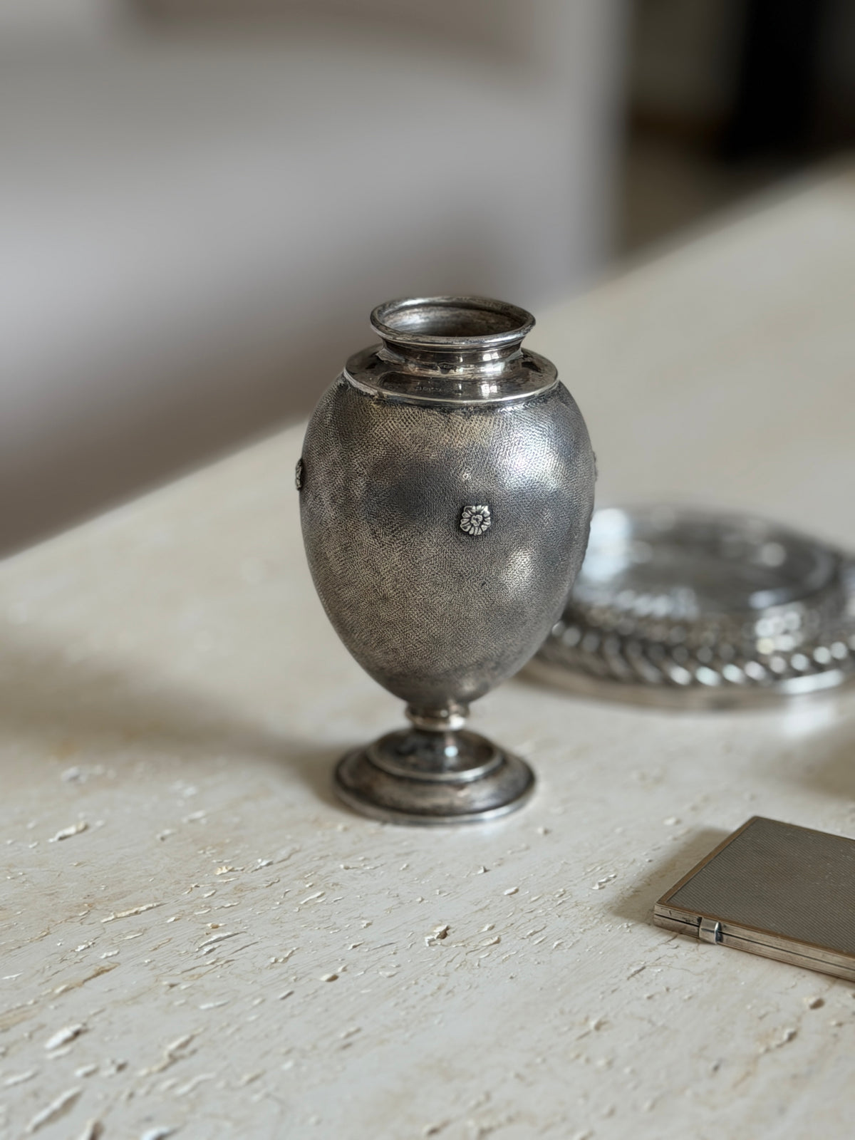 Mario Buccellati vase with rosettes and a stepped round foot on travertine, a silver cigarette case and chain coaster beside