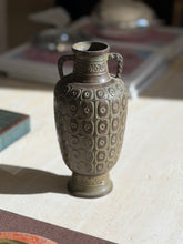 Close view of the geometric relief on the bronze vase, the green and russet patina highlighting each raised square and ring