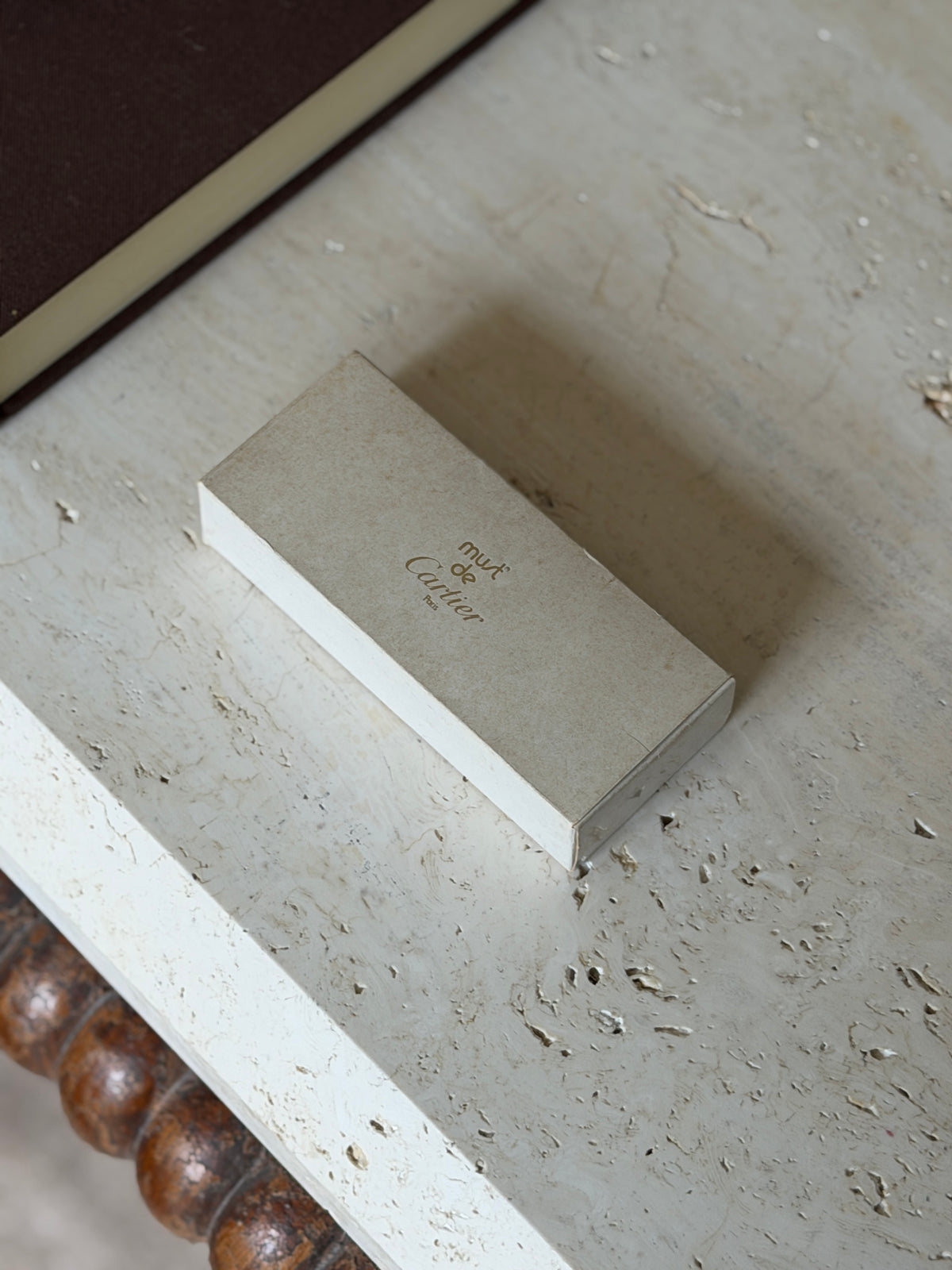 Original cream must de Cartier Paris outer box with gold lettering on a travertine table near a brown book