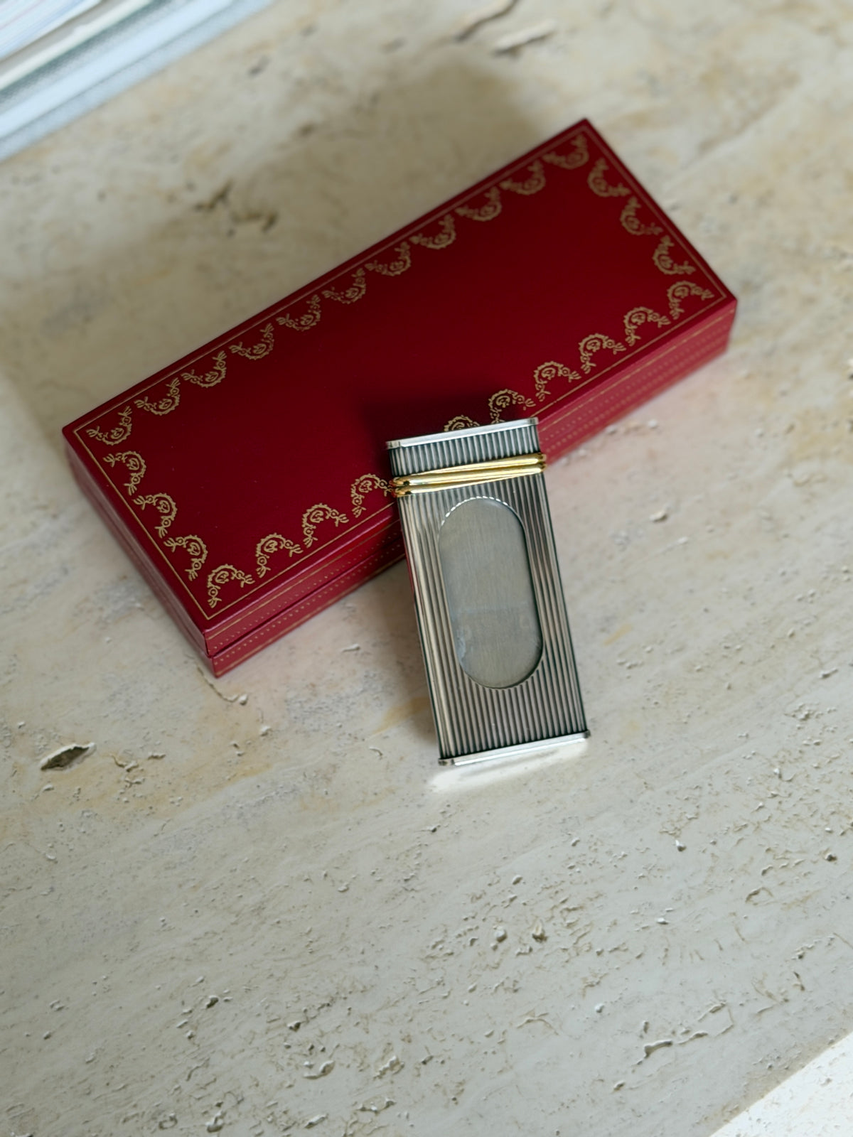 Fluted silver tone Cartier cigar cutter with twin gold bands and an oval cutting window, laid against its red garland case