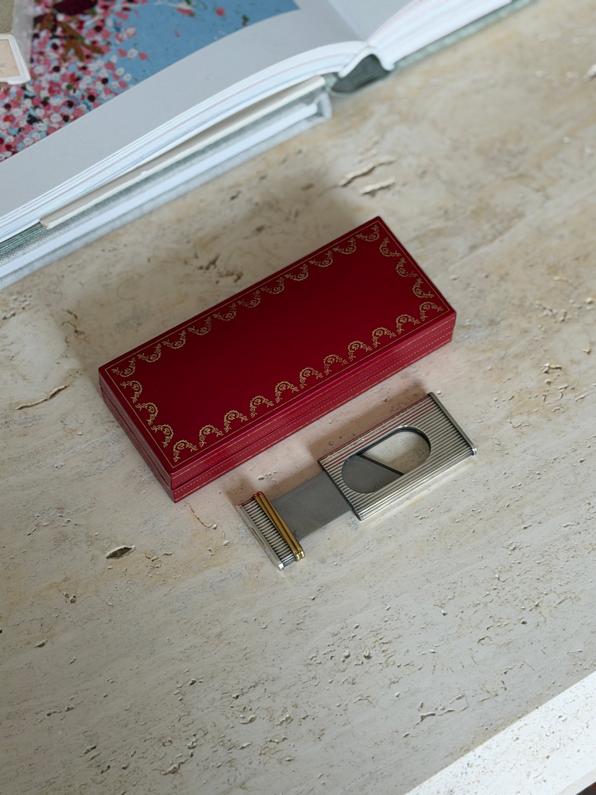 Cartier cigar cutter slid open beside its red case, the steel blade crossing the oval opening between the fluted halves
