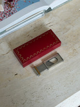 Cartier cigar cutter slid open beside its red case, the steel blade crossing the oval opening between the fluted halves