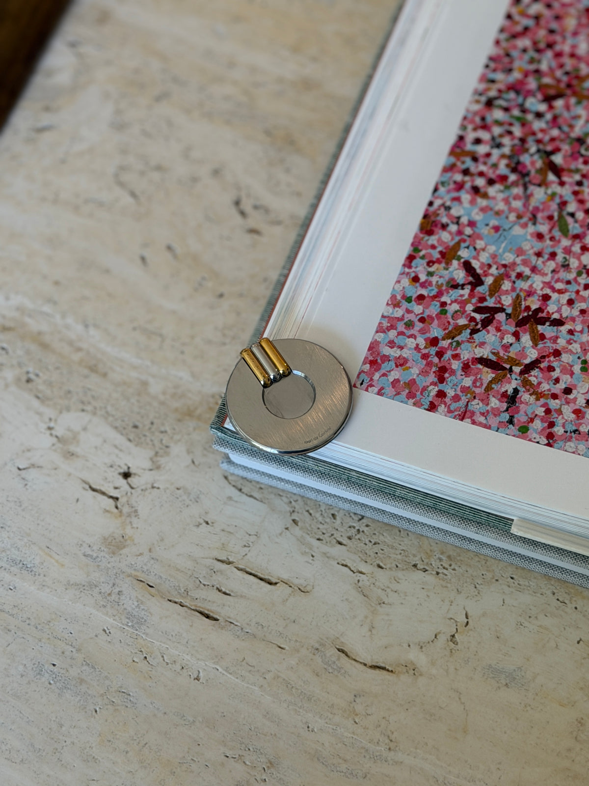 Round Cartier cigar cutter resting at a book corner on travertine, the gold, silver and gold bars above the circular opening