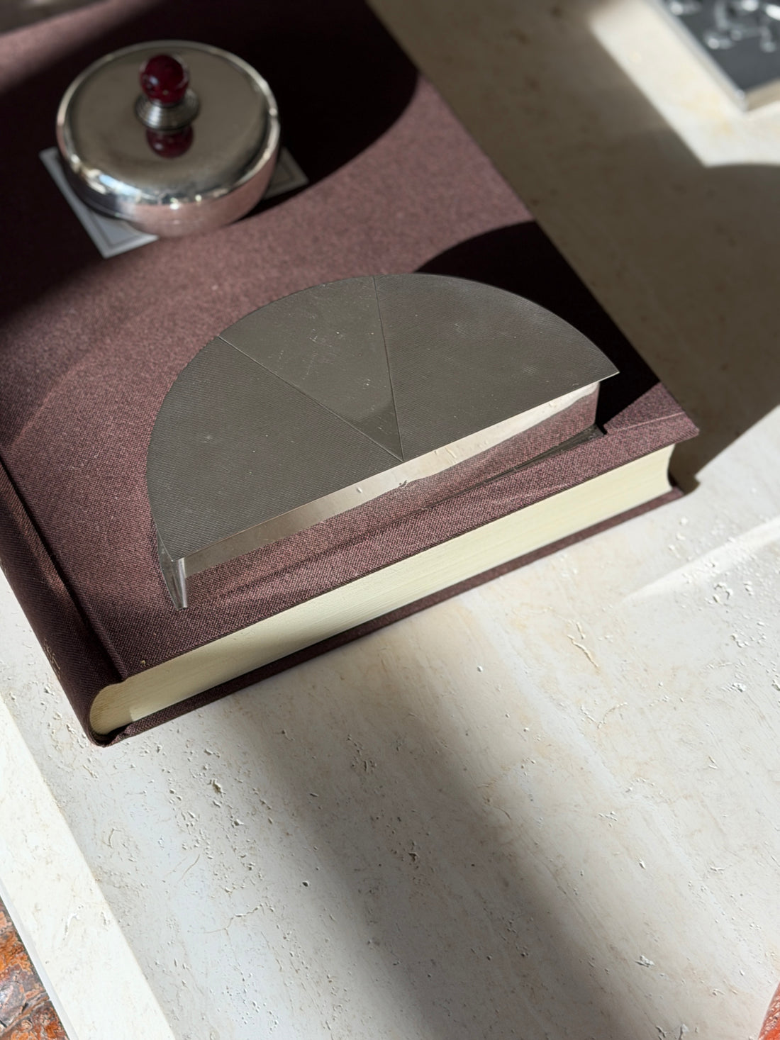 Olivetti half moon box in engine turned silver plate on a brown clothbound book, the lid divided into three textured sectors, a lidded silver box behind