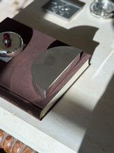 Angled view of the semicircular Olivetti box on the Superfine Tailoring Black Style book, the fan of engine turned panels catching sunlight
