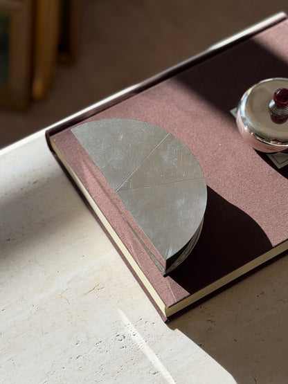 Overhead view of the Olivetti demilune box on a rose brown book, fine diagonal guilloche lines running across each sector of the lid