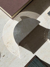Top down view of the half round engine turned box on travertine, its reflected light arcing across the stone beside a chain link coaster