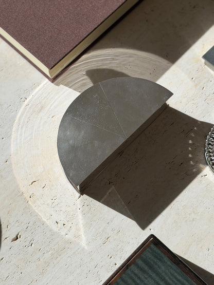 Top down view of the half round engine turned box on travertine, its reflected light arcing across the stone beside a chain link coaster