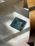 Collectors Gene vintage patinated solid bronze square vide poche tray on stone tile floor with dramatic sunlight