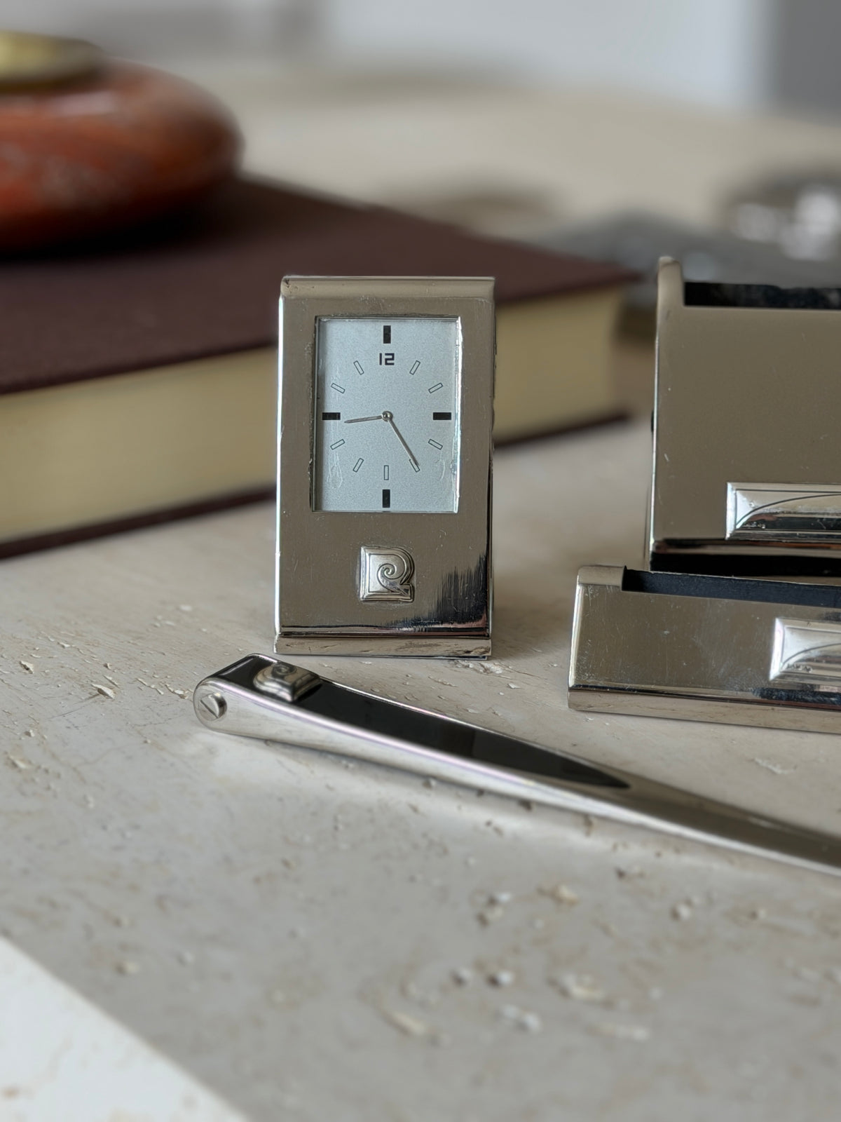 Close up of the Pierre Cardin desk clock, a silver dial with black baton markers and a bold 12 above the raised spiral logo