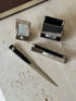 Close overhead view of the Pierre Cardin pieces, showing the black lined pen tray, spiral logo plaques, and long pointed letter opener blade