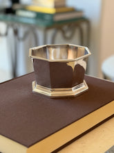 Ralph Lauren octagonal silver bowl on a brown book atop a console, a stack of books and a glass table blurred behind