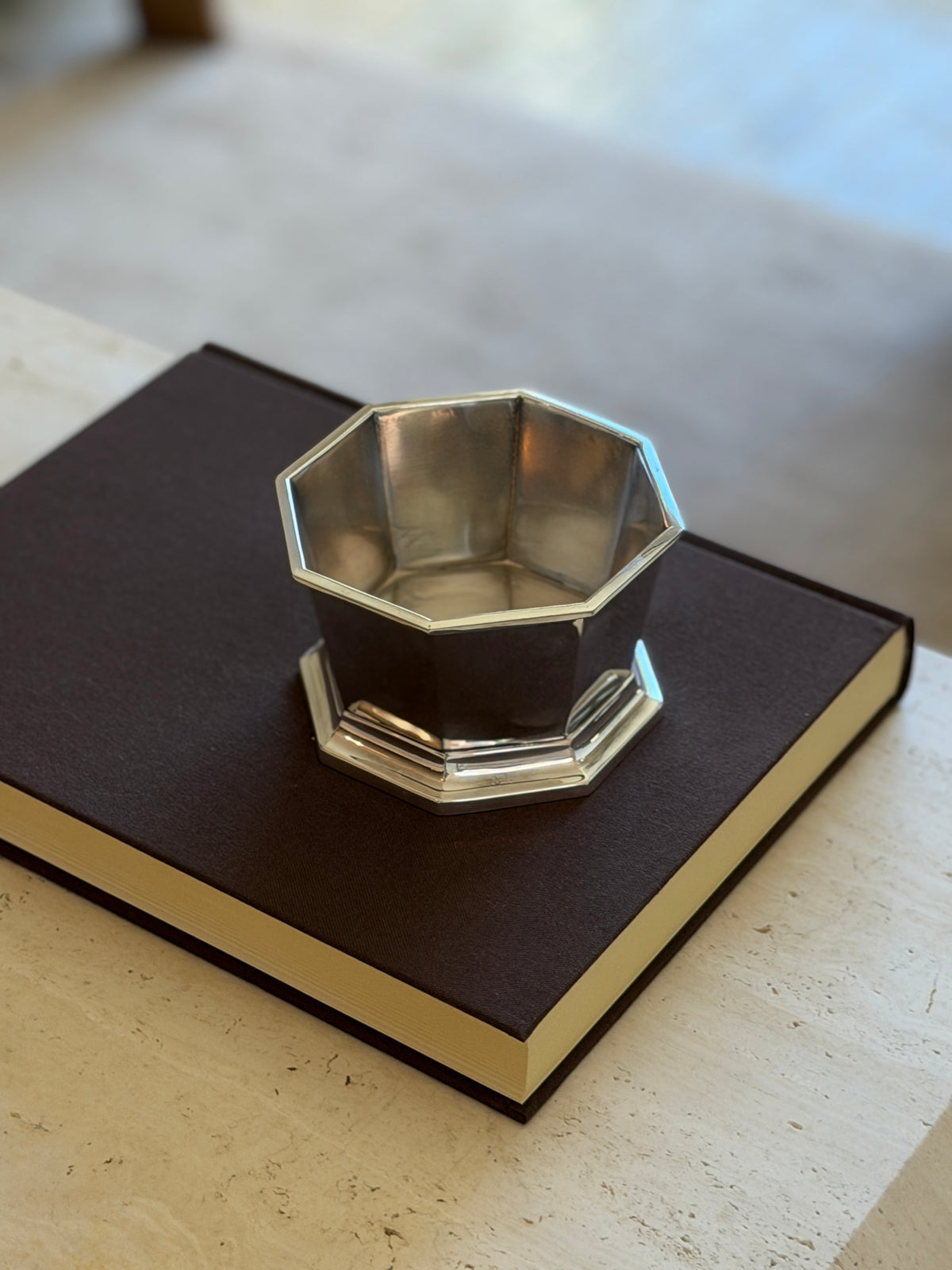 High angle view of the eight sided nut bowl on a brown book resting on travertine, the polished interior catching daylight