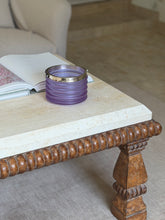 The bucket displayed on a stone-topped coffee table with a carved wooden leg, an open book beside it in a living room setting