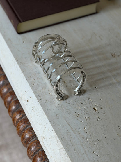 Silver plated horseshoe toast rack on a travertine table, nail studded horseshoe ends joined by curved wire dividers and a horseshoe handle
