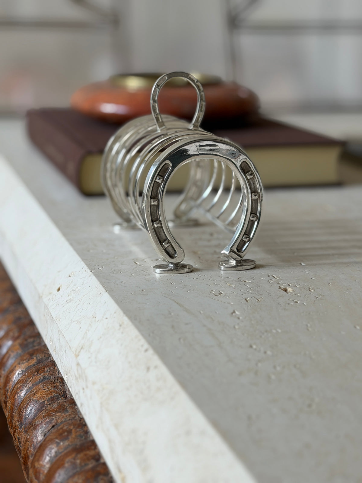 English horseshoe toast rack along the travertine table edge, a brown book and red ashtray behind the loop handle