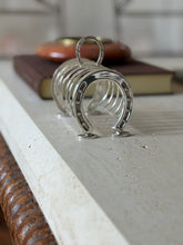 English horseshoe toast rack along the travertine table edge, a brown book and red ashtray behind the loop handle