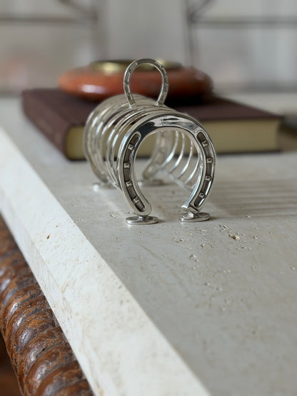 English horseshoe toast rack along the travertine table edge, a brown book and red ashtray behind the loop handle
