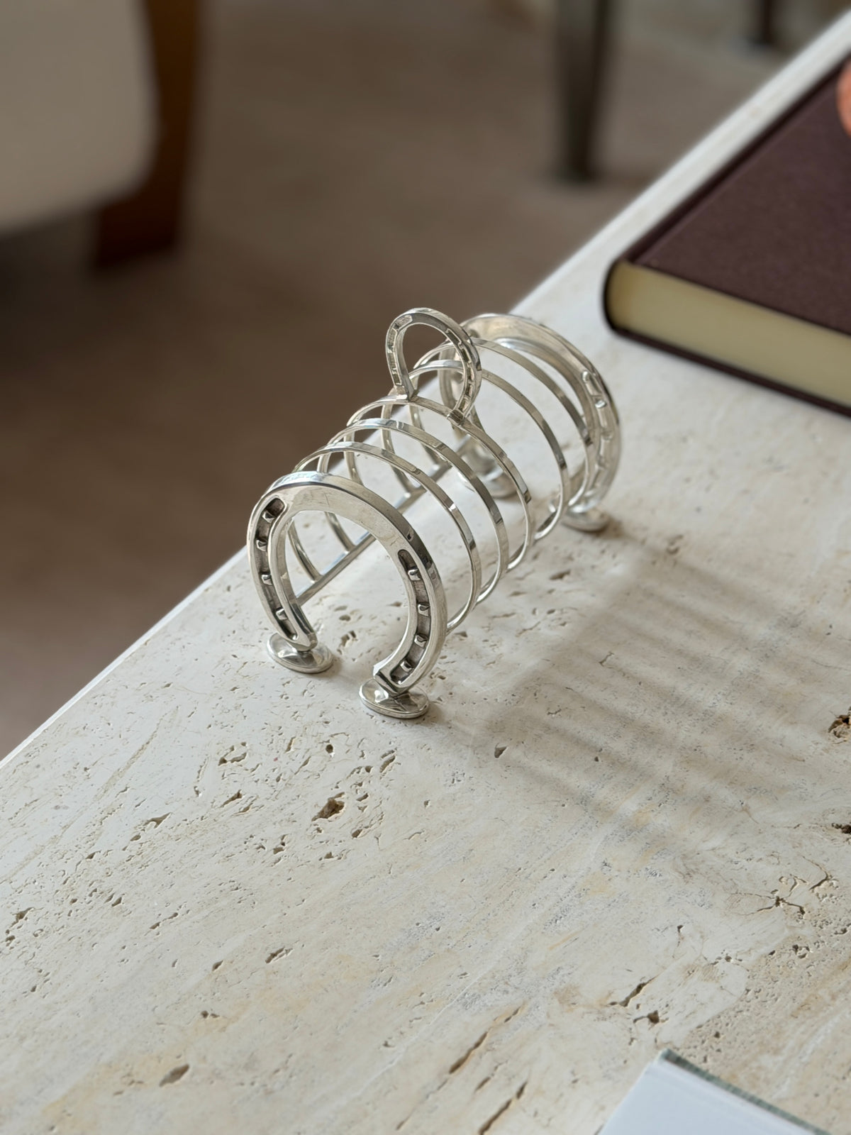Angled view of the horseshoe toast rack from the far end, the arched dividers casting striped shadows on travertine