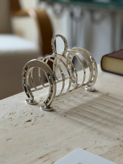 Silver plated toast rack with horseshoe ends and loop handle in soft light, a bentwood chair blurred in the background